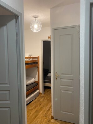 Ein schmaler Korridor mit einem Holzbett, einer weißen Tür und einer Deckenleuchte.