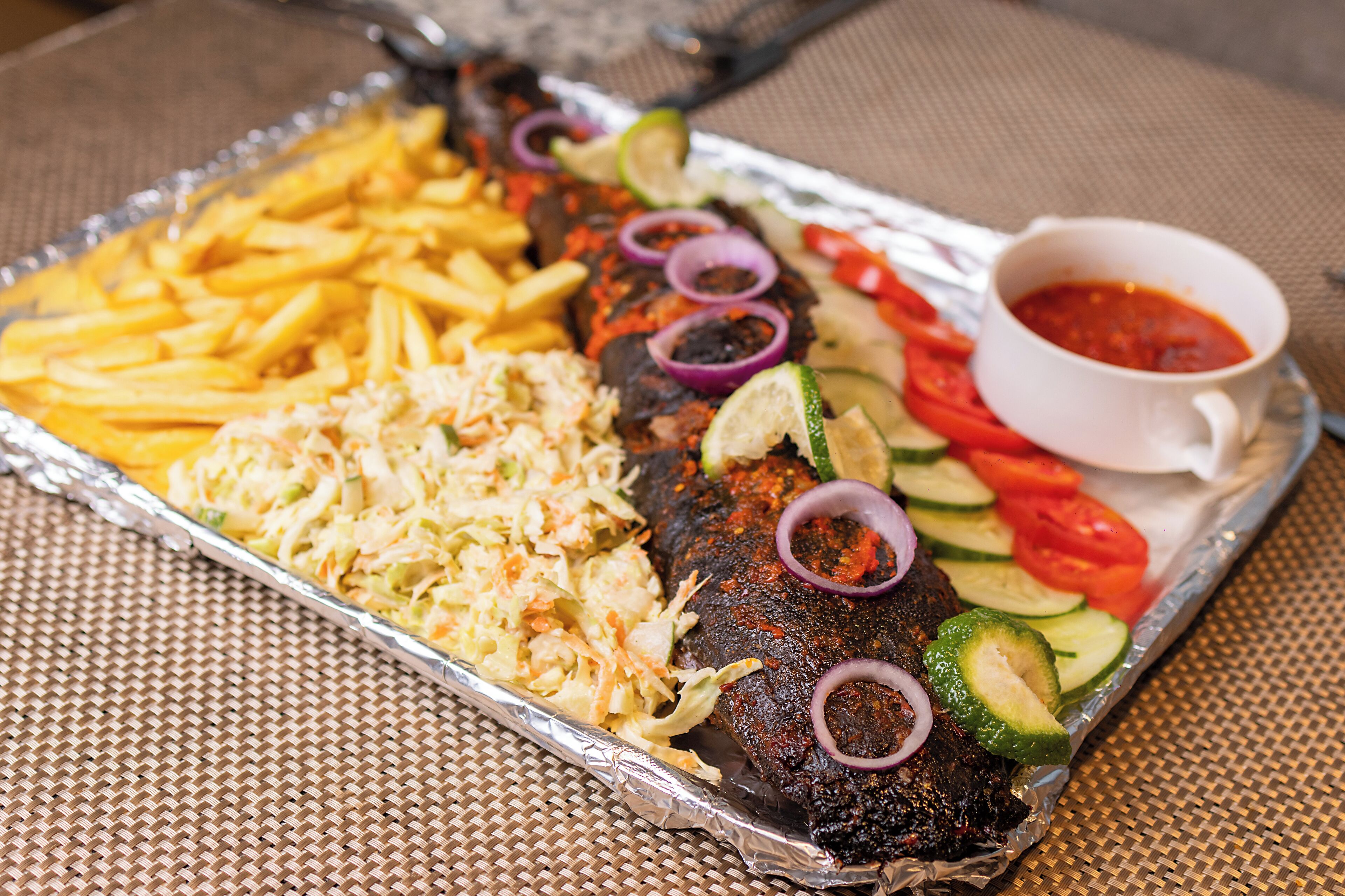Een maaltijd met frietjes, een salade van zuurkool, gegrild vlees, gesneden groenten en een portie saus op een tafel.