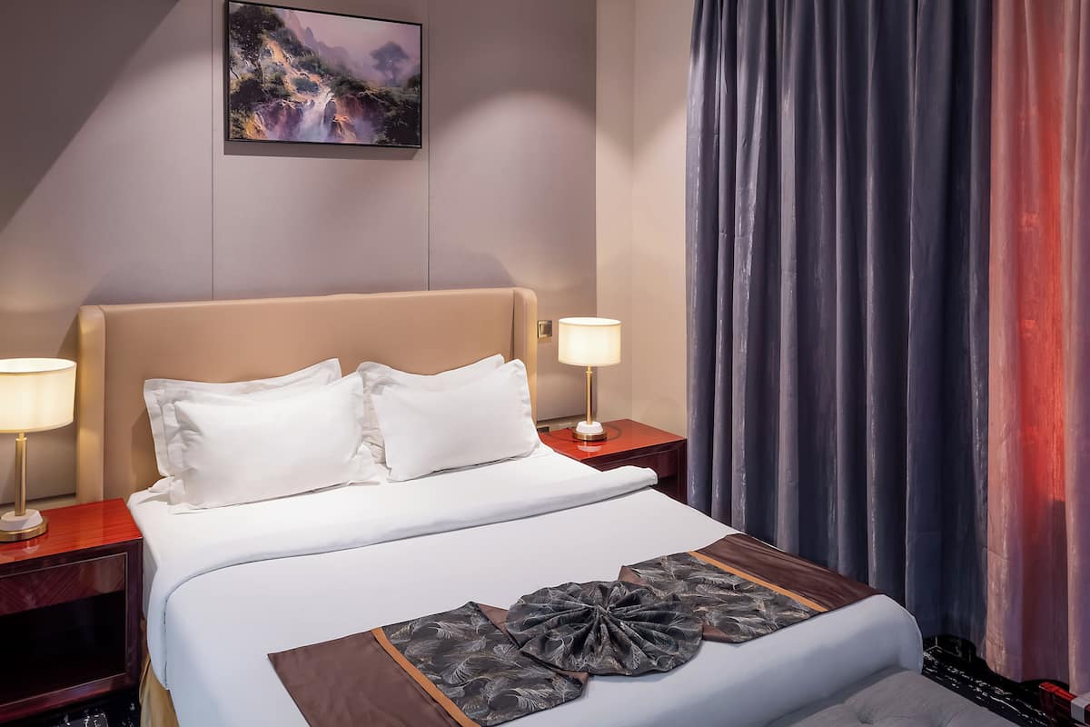 Habitació d'hotel amb un llit, dues làmpades de nit, una tauleta de nit, un quadre a la paret i una cortina.