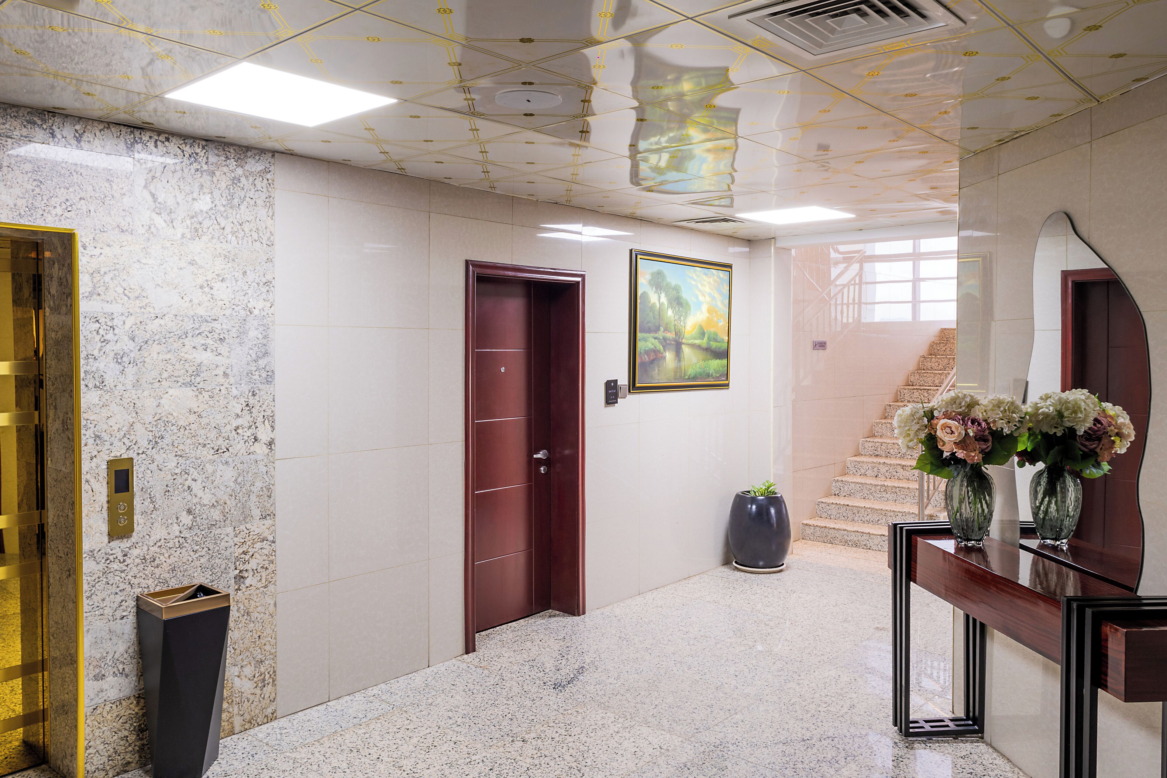 A lobby with marble walls, a wooden door, a staircase, and a console table with vases.