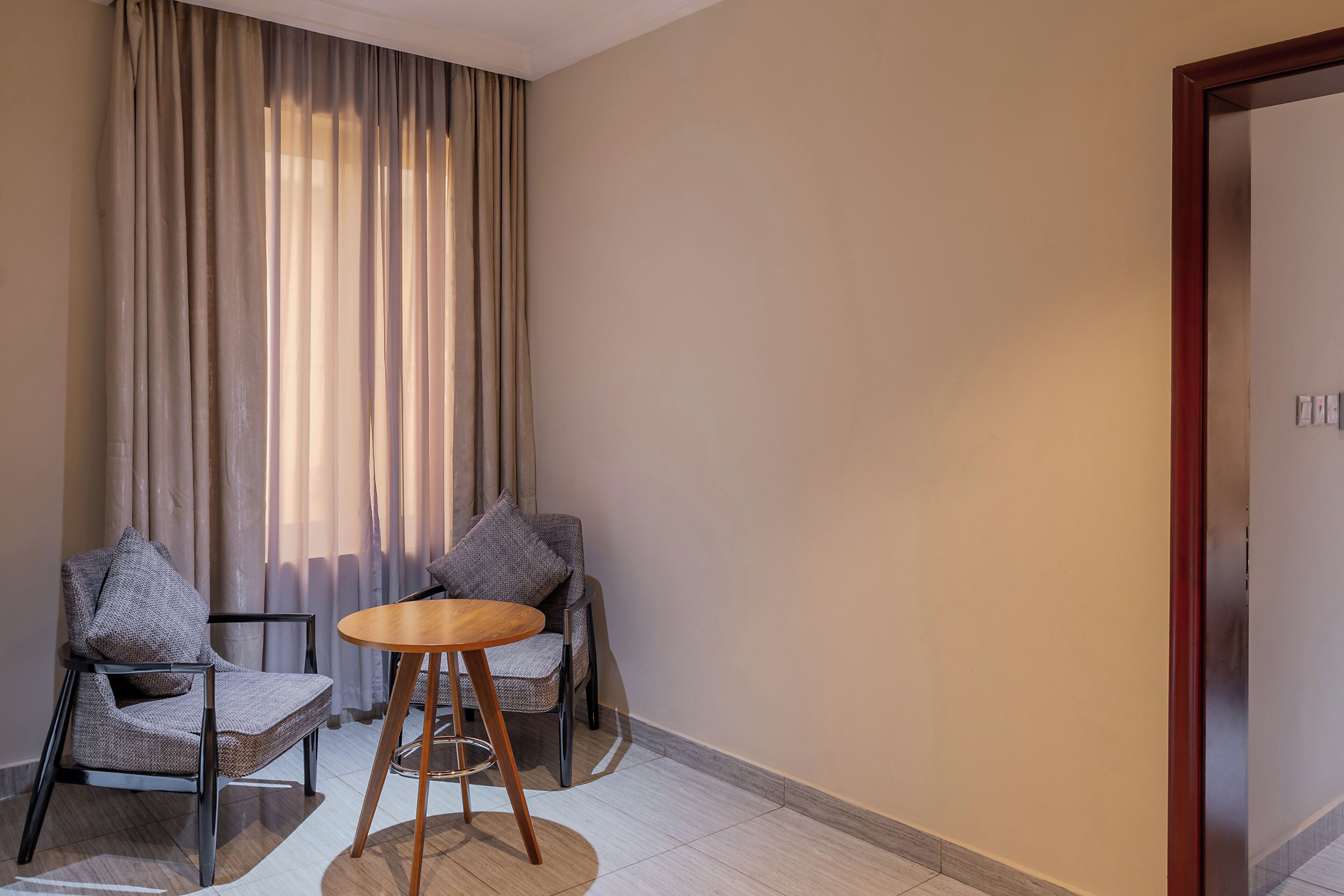 A room with two chairs, a small wooden table, and a large window with curtains.