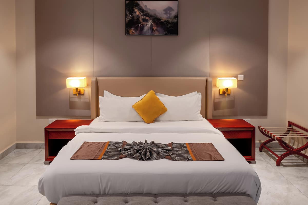 Habitació d'hotel ordenada amb un llit, dues làmpades de nit, un quadre a la paret i una cadira de fusta.
