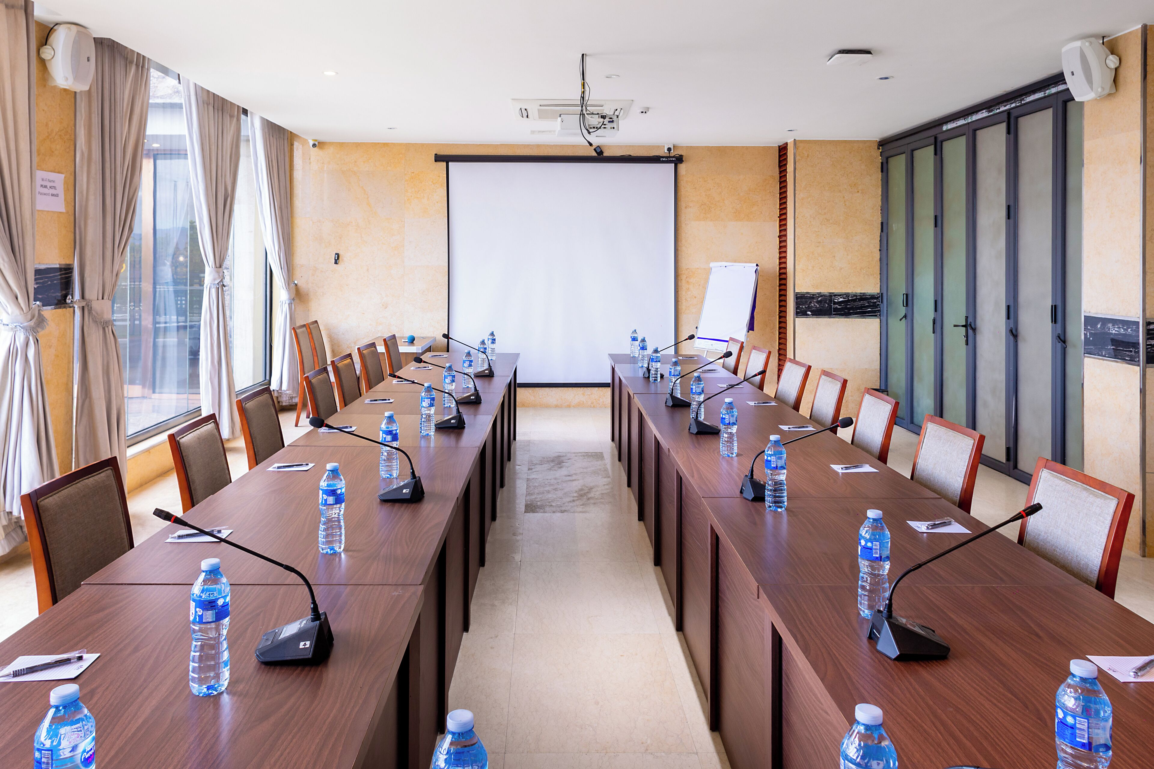 A conference room with a long table, chairs, microphones, and water bottles.