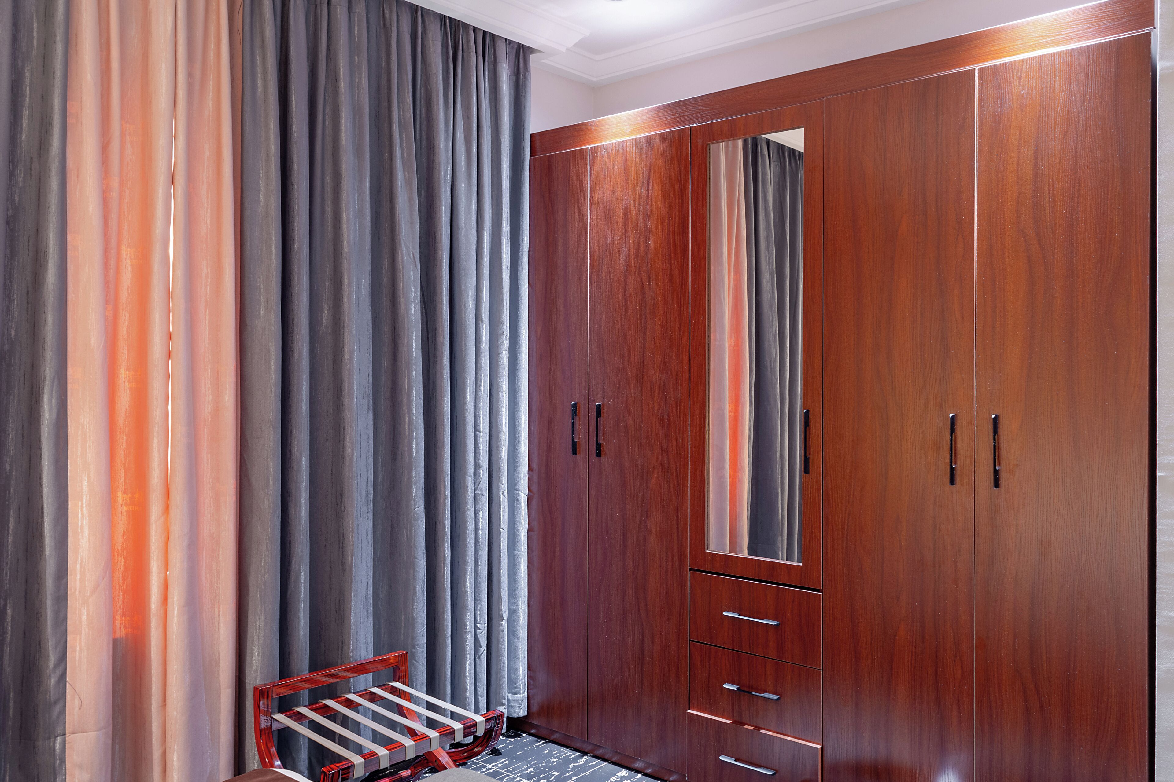 A room with a large wardrobe, a bench, and a mirror.