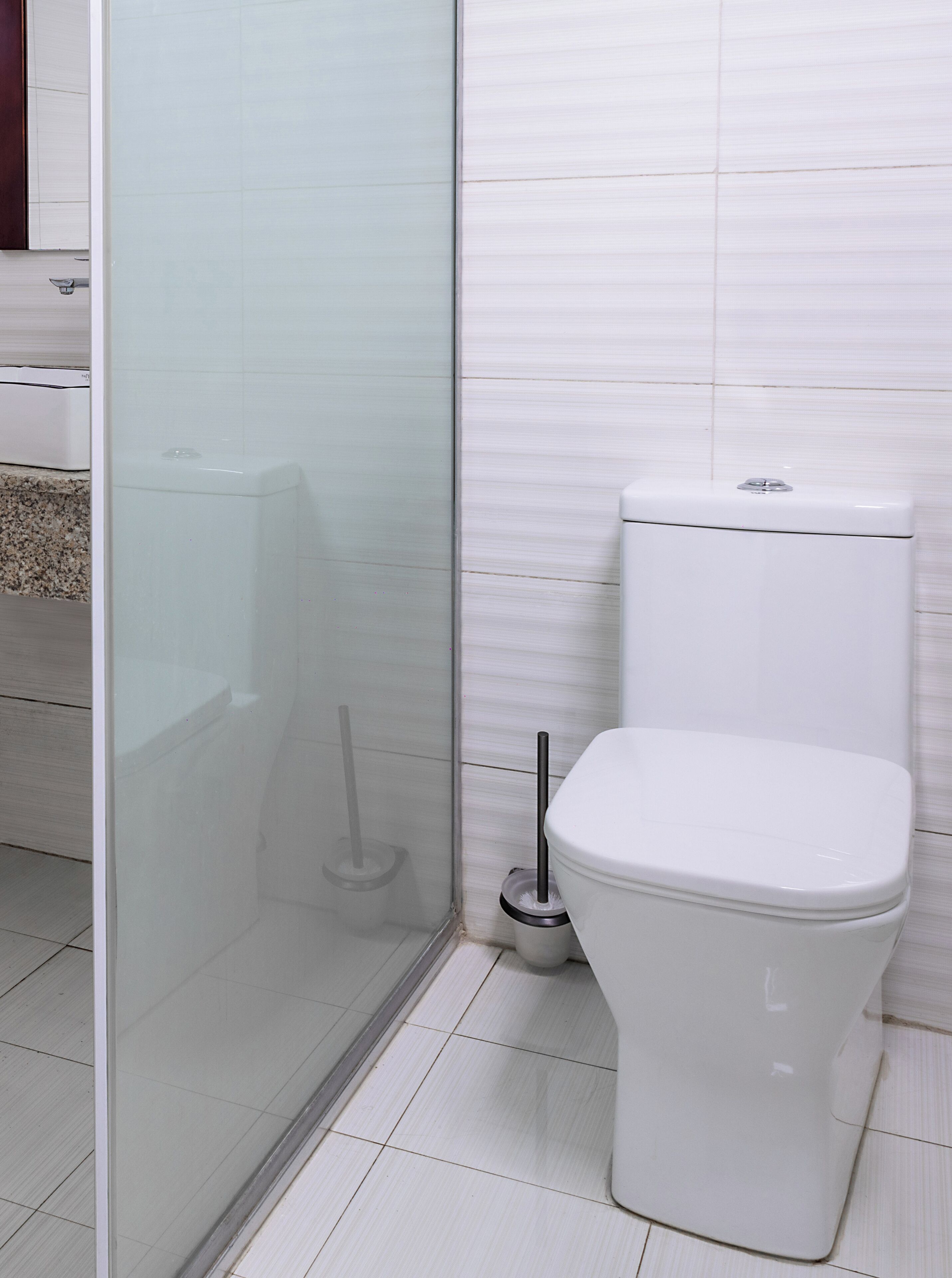 A bathroom with a white toilet, a glass shower enclosure, and a tiled floor.