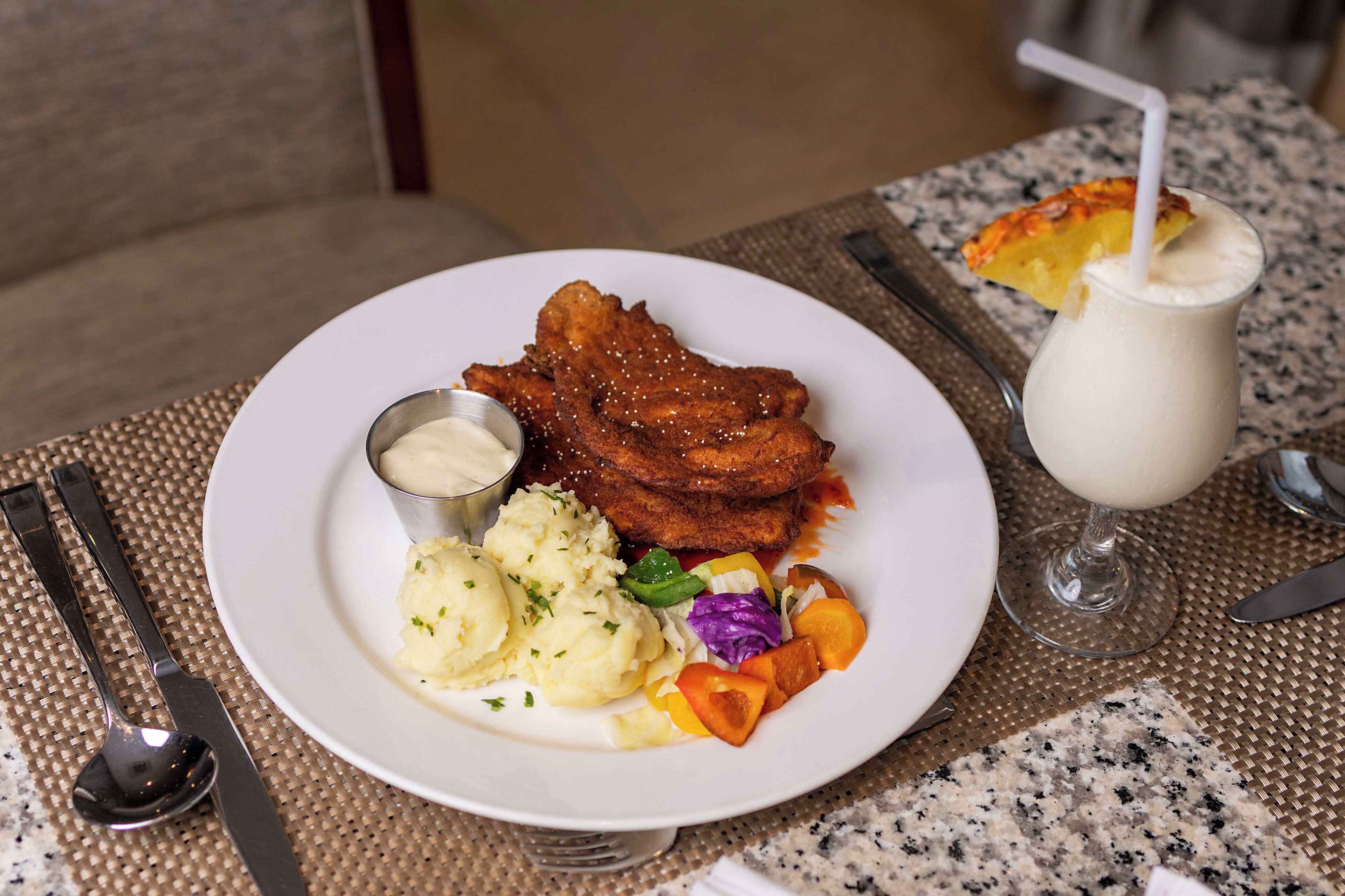 Une assiette contenant du poulet frit, de la purée de pommes de terre et une salade, le tout posé sur une table recouverte d’un set de table.