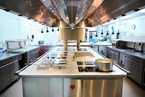 Een commerciële keuken met roestvrijstalen apparatuur, een centraal eiland met een pan, en verlichting.