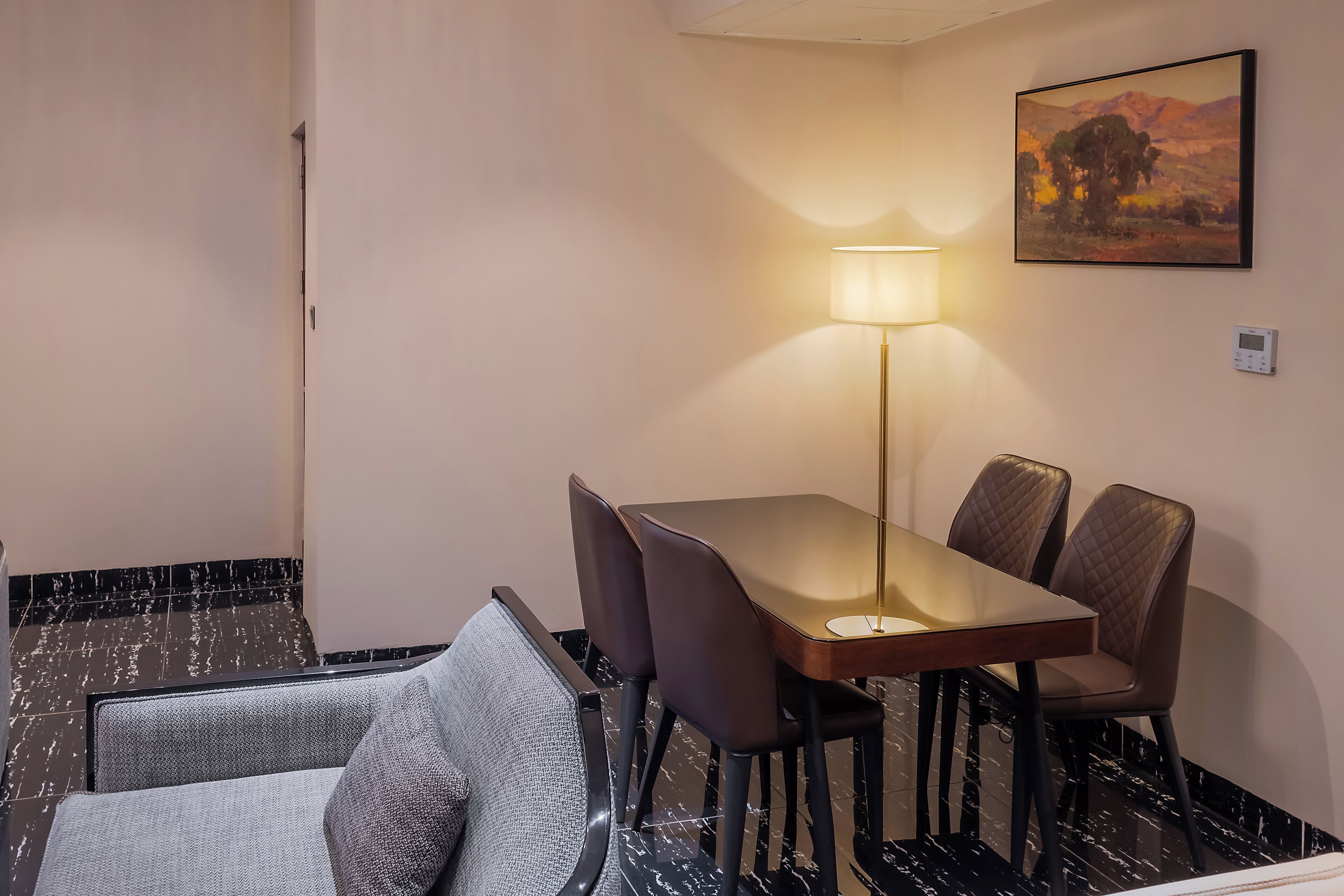Een hotelkamer met een eettafel, stoelen, een bank, een lamp en een schilderij aan de muur.