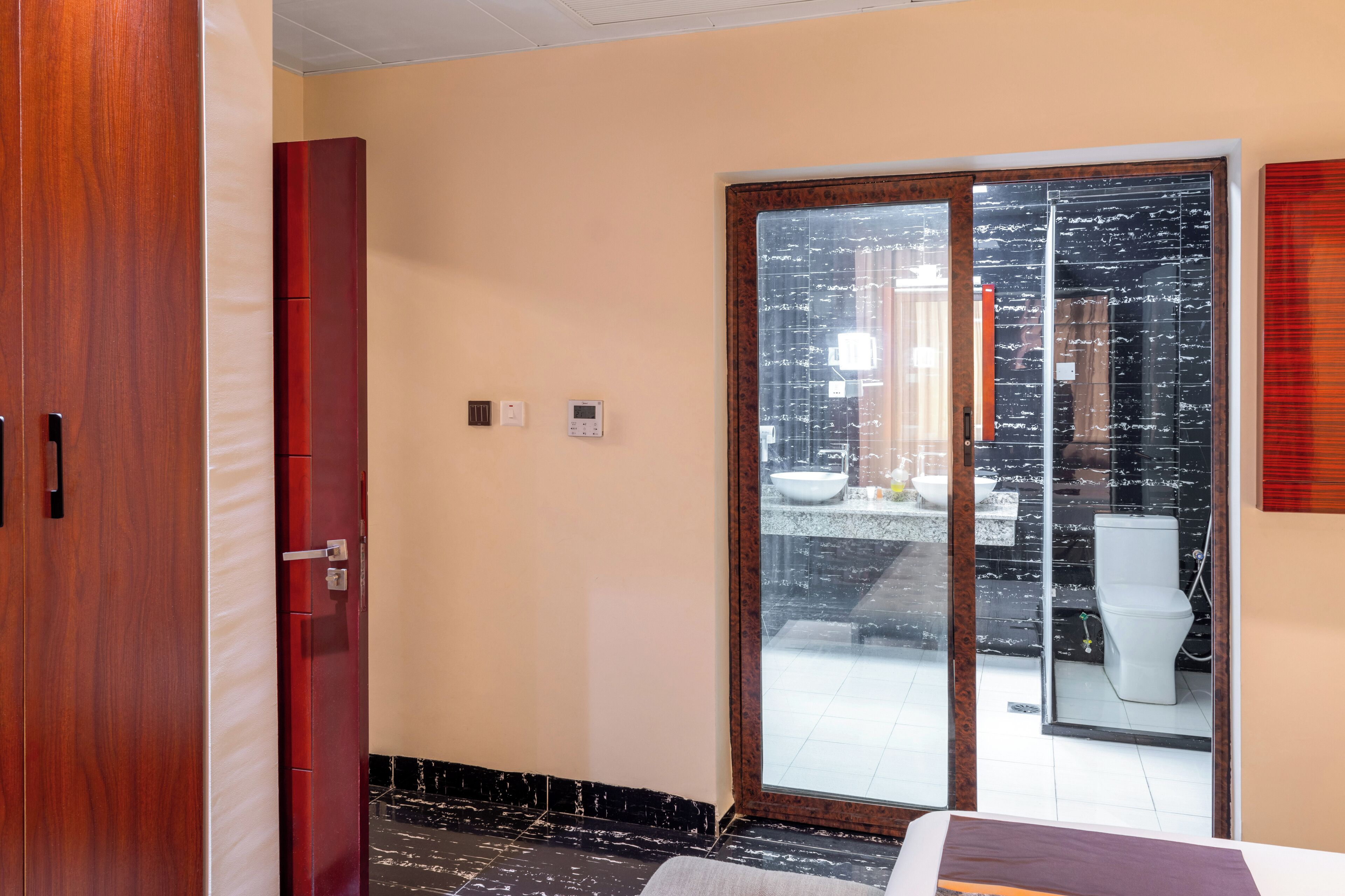 A hotel room with a wooden wardrobe, a sliding glass door leading to a balcony, and a bathroom visible through the door.