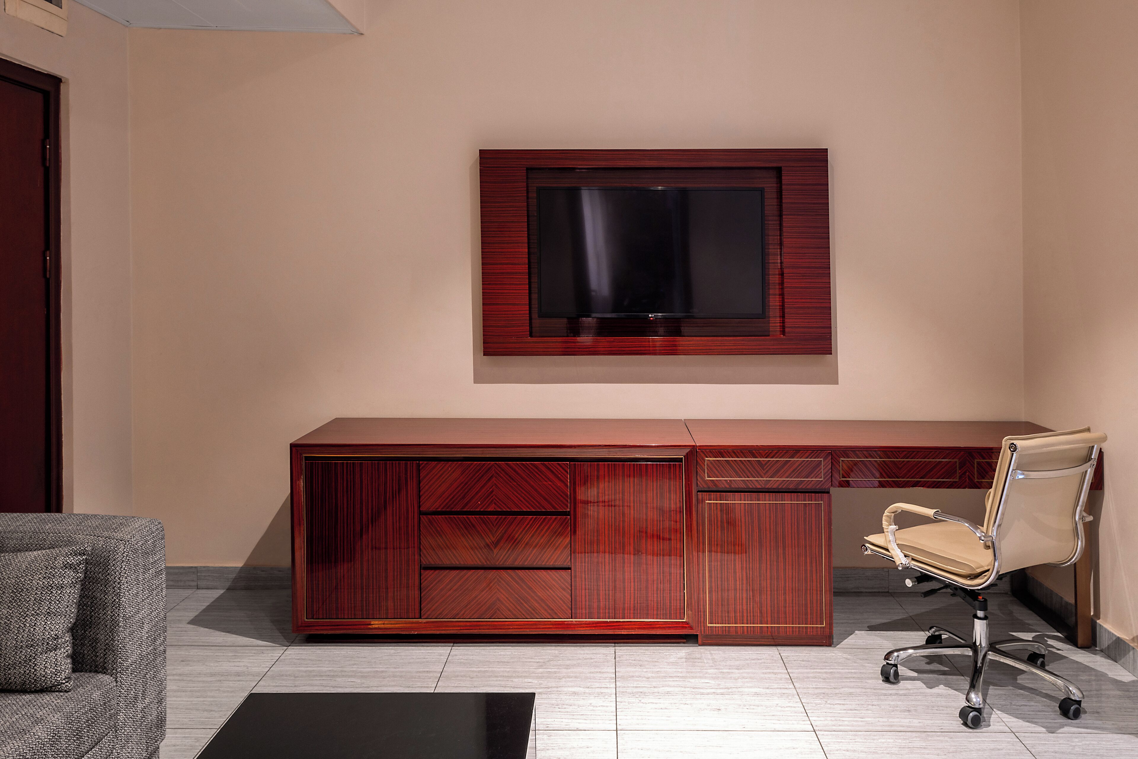 A modern office space with a large wooden desk, a leather office chair, and a mounted flat-screen TV.