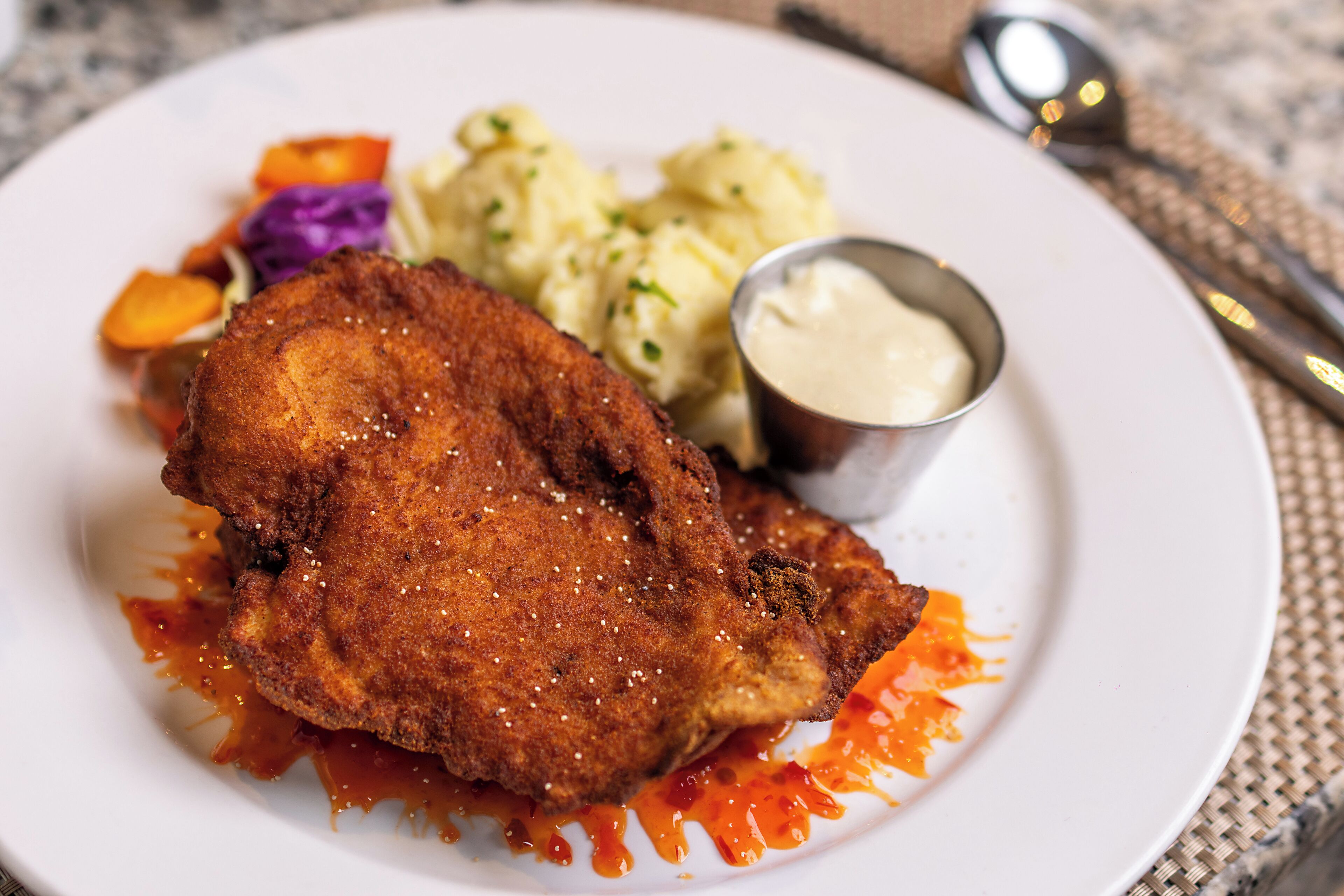 A plate with a breaded and fried item, possibly chicken, accompanied by mashed potatoes and a small bowl of sauce.
