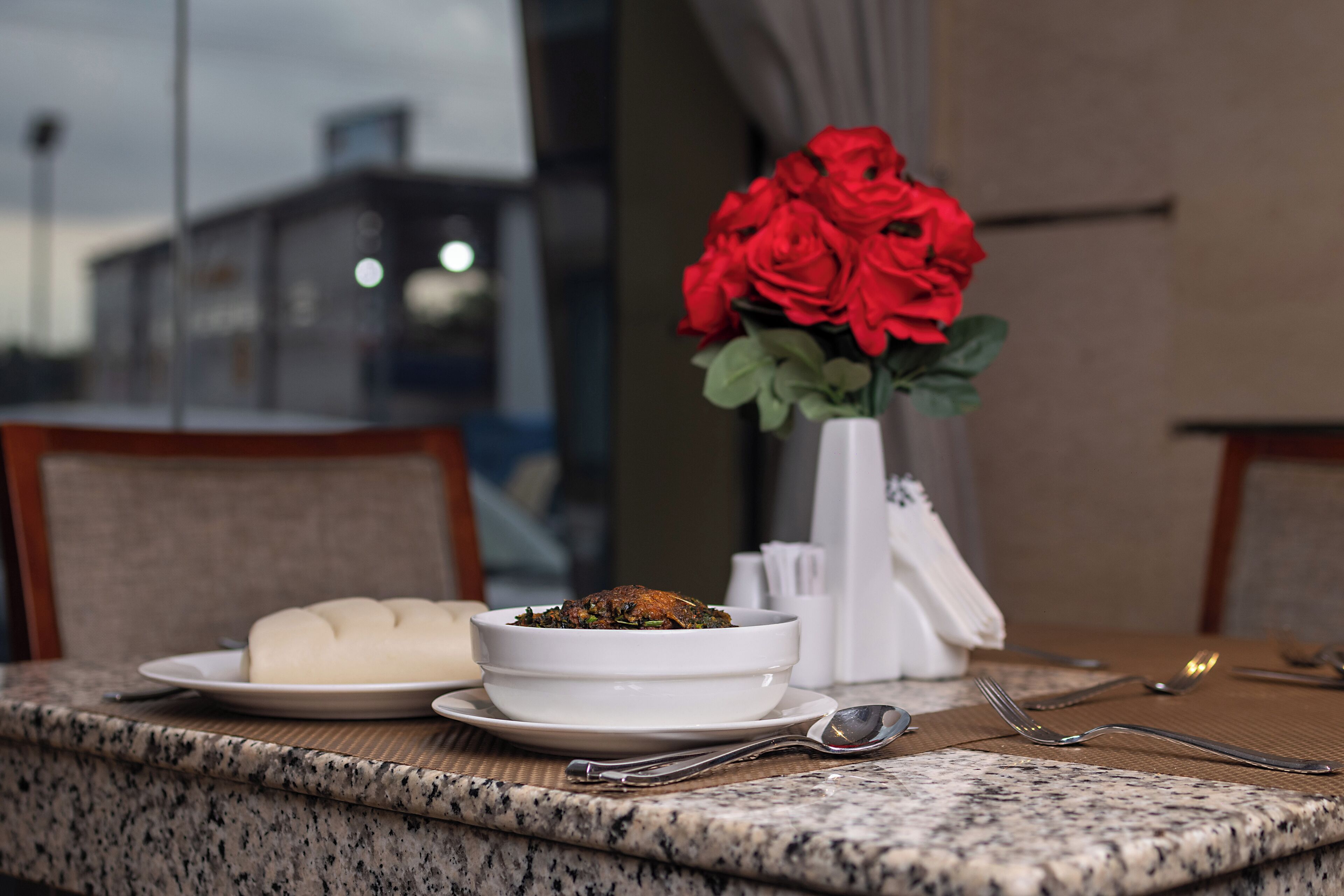 A dining table with a bowl of food, a plate of dumplings, and a vase of red roses.