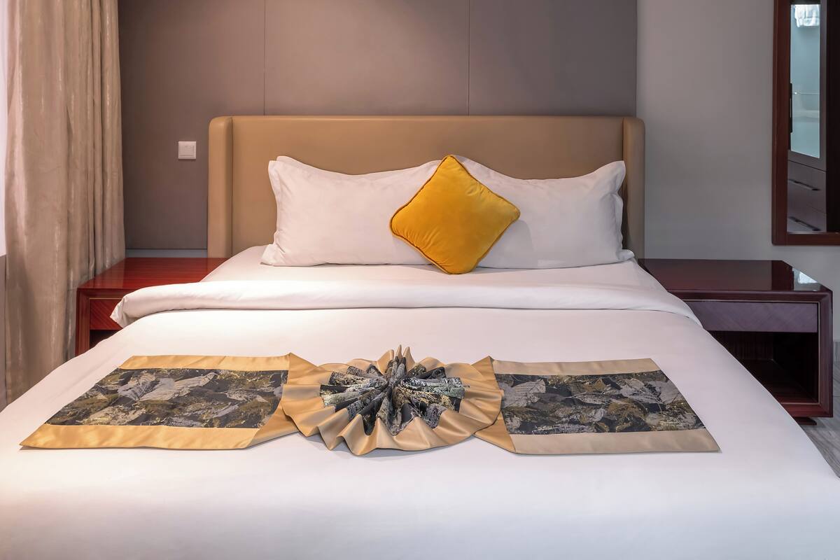 Una habitació d'hotel amb llit, una taula de nit, un mirall i una finestra amb cortines.