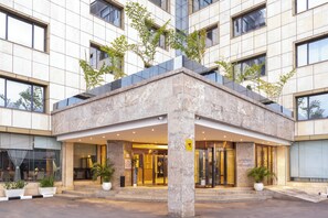 Una entrada de hotel moderna con fachada de piedra, ventanas amplias y plantas en macetas.