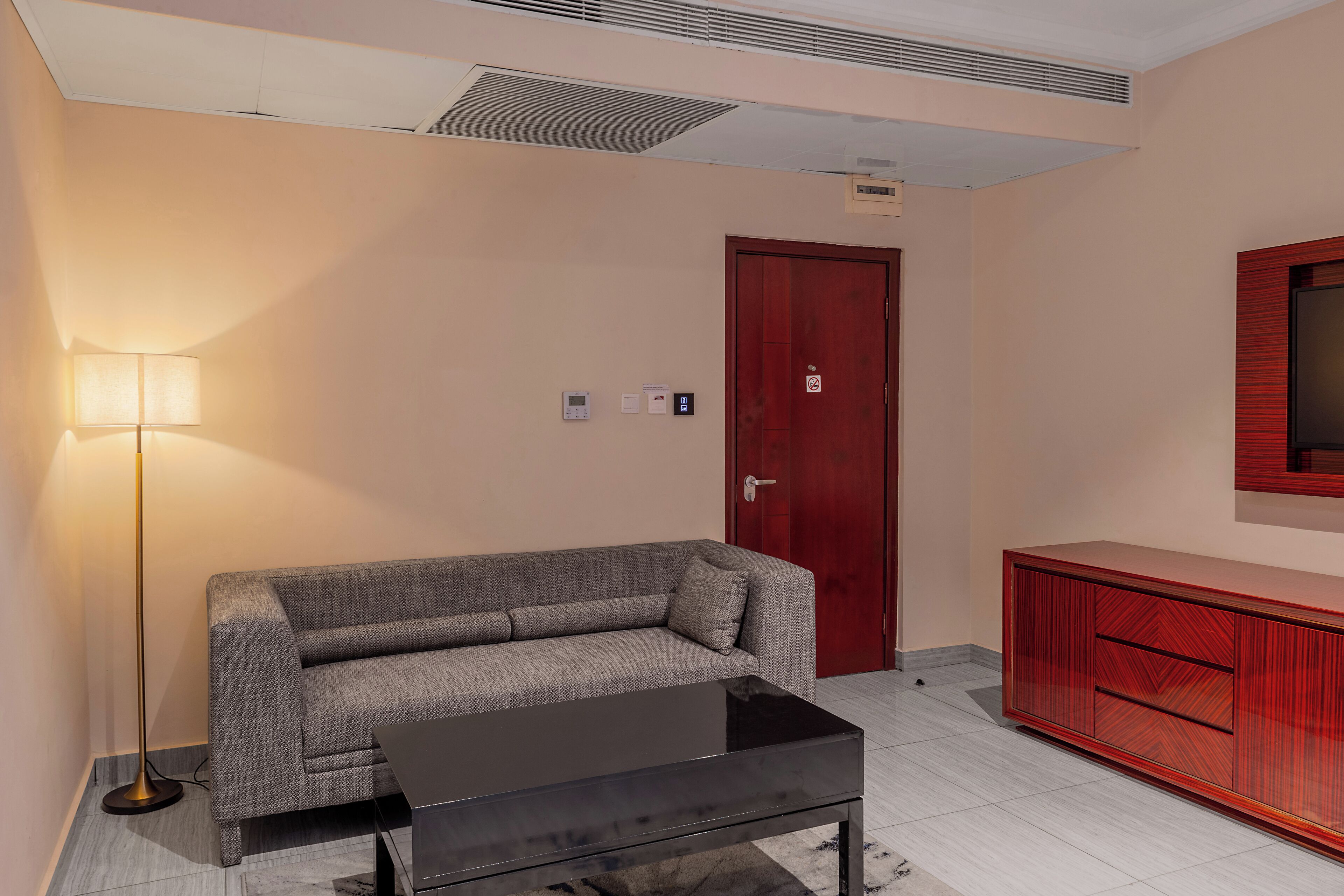 A modern living room with a sofa, a coffee table, a floor lamp, a red door, and a wooden cabinet.