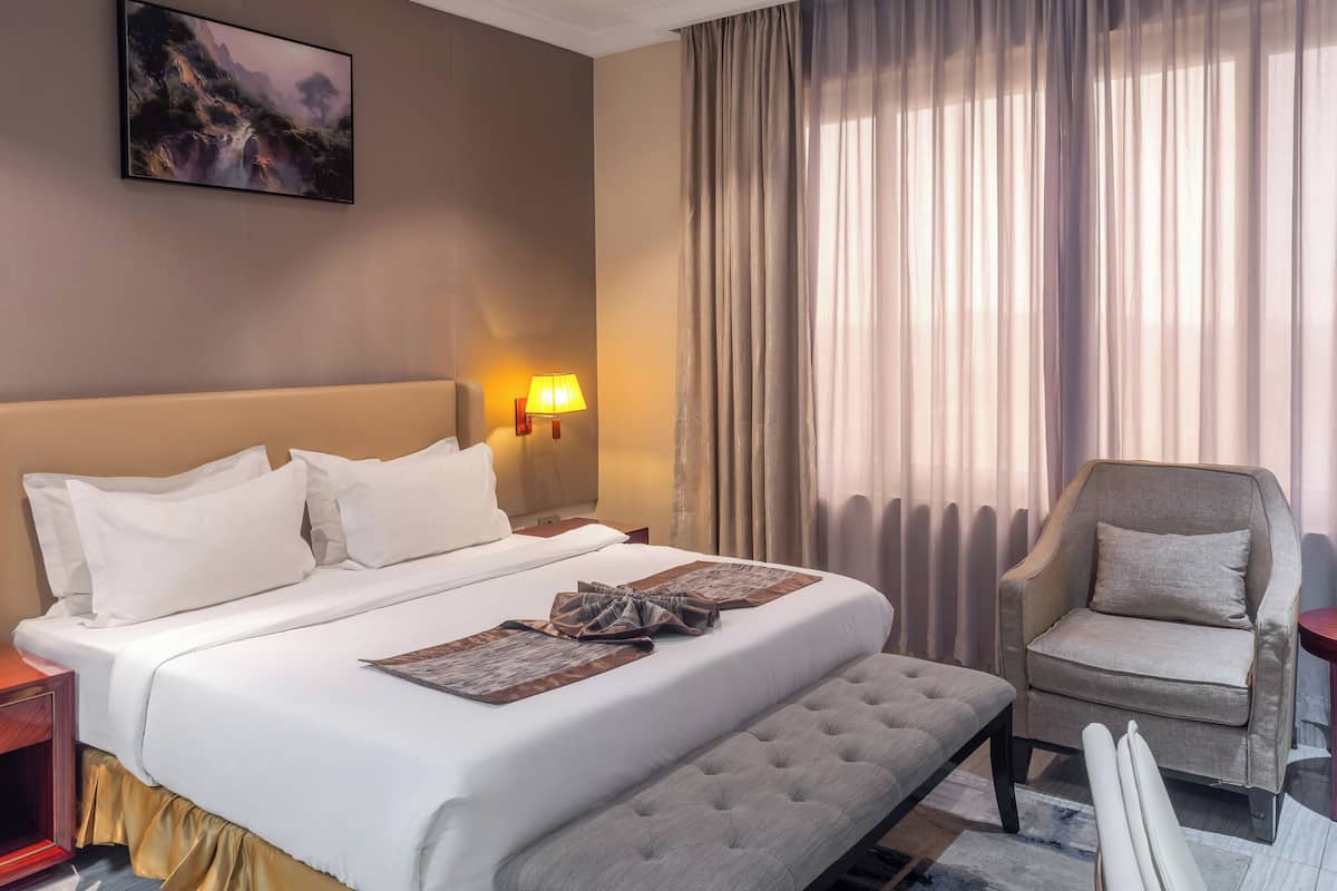 Una habitació d'hotel amb un llit gran, una cadira, una tauleta de nit i un quadre a la paret.