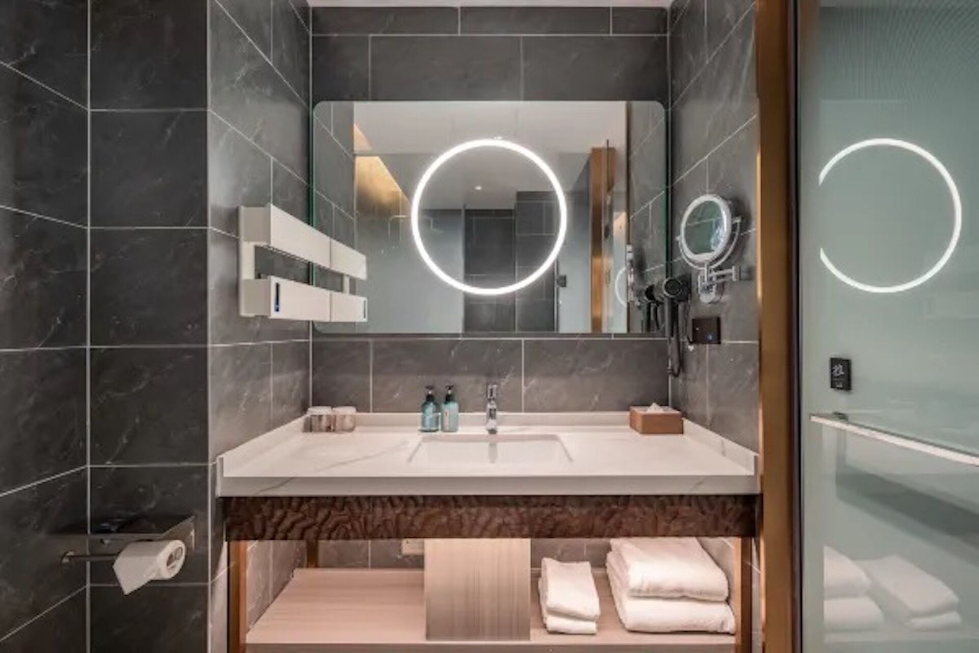 A modern bathroom with a large mirror, built-in shelves, a vanity with a sink, and a towel rack.
