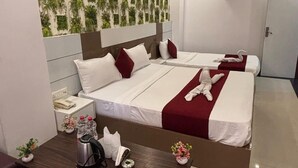 Ein Hotelzimmer mit zwei Betten, einem Holztischchen, einem kleinen Tisch mit Wasserkocher und einer Vase sowie einer Wand mit grünem Blattmuster.