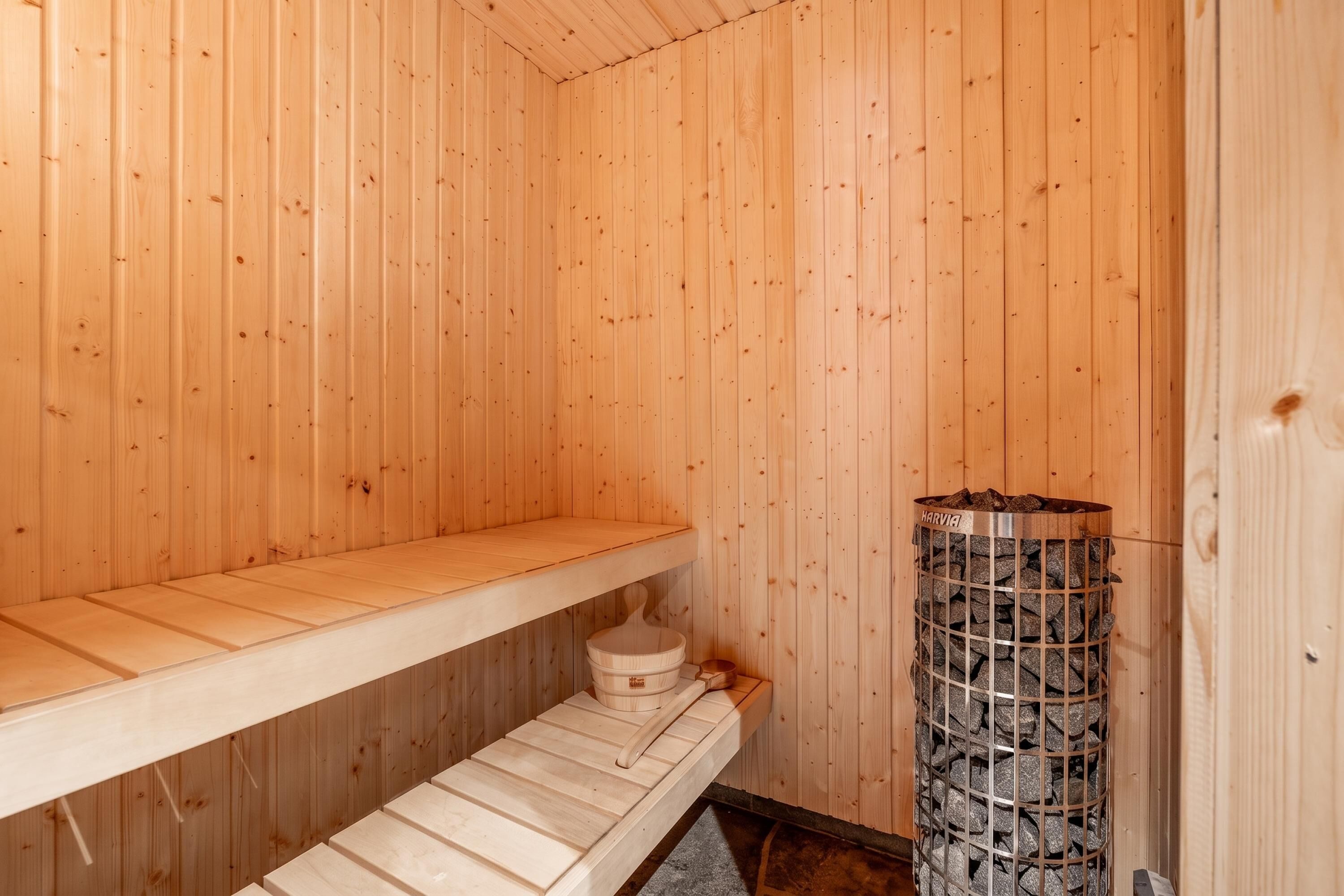 A sauna room with wooden walls, a bench, a small table, and a metal container with rocks.