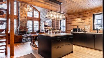 A modern kitchen with a stone fireplace, wooden beams, and large windows.