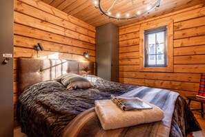 A cozy log cabin bedroom with a bed, a window, and a ceiling light fixture. - Idre Luxury Chalet Winter Haven /w Sauna (Idre)