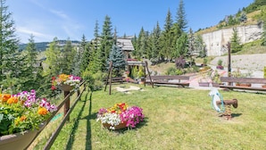 Un jardin avec des parterres de fleurs, une balançoire en bois et une aire de jeux.