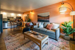 A cozy living room with a sofa, coffee table, and a dining area with chairs. - Downtown BOHO condo. Walk to Branson Landing. Pool/Fitness Center (Branson)