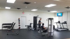 Ein Fitnessstudio mit verschiedenen Trainingsgeräten, darunter Laufbänder, Kraftgeräte und Kurzhanteln.