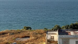 Μια παραθαλάσσια θέα με καθαρό ουρανό, ήρεμη θάλασσα και ένα κτίριο με επίπεδη στέγη και ένα μικρότερο κτίσμα στα δεξιά.