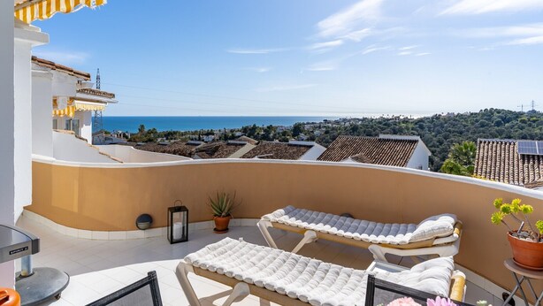 Un balcon avec deux chaises longues, un pot de fleurs, une lanterne et une vue sur la mer et la ville.