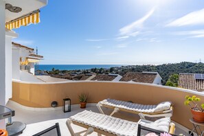 Ein Balkon mit zwei Liegestühlen, einem Blumentopf, einer Laterne und Blick auf das Meer und die Stadt.