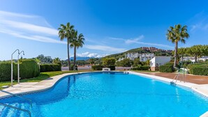 Une piscine d’un bleu éclatant, avec un espace aménagé au bord, des palmiers et une vue sur les bâtiments en arrière-plan.