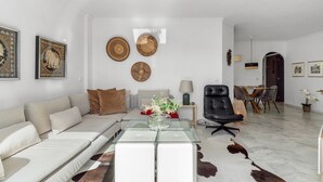 Un salon moderne comprenant un canapé, une table basse en verre, un fauteuil en cuir et un coin repas avec une table et des chaises.