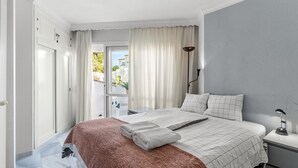 Une chambre à coucher avec un lit, une table de chevet, une lampe et une vue sur l’extérieur.
