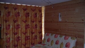 Une pièce avec un mur en bois, un canapé recouvert d’un tissu à motifs floraux, une table ronde avec une nappe à motifs floraux et une chaise en bois.