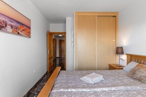 A hotel room with a bed, a wooden door, a nightstand, a lamp, and a painting on the wall.