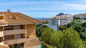 A multi-story building with a tiled roof, balconies, and a view of the sea.