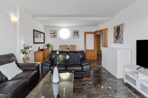 A modern living room with a black leather sofa, a glass coffee table, and a white cabinet.