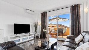 A modern living room with a flat-screen TV, leather sofa, and a glass coffee table.