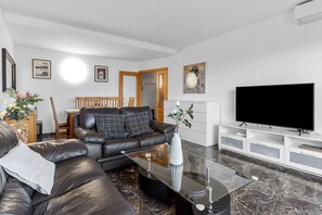 A modern living room with a leather sofa, a glass coffee table, a flat-screen TV, and a white entertainment unit.