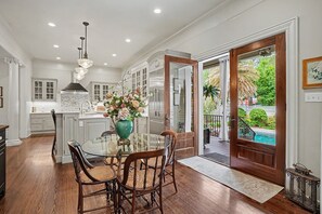 A dining area with a glass table, chairs, and a vase of flowers. - Luxury Savannah Estate w/ Heated Pool, Manicured Gardens by Lucky Savannah (Savannah)