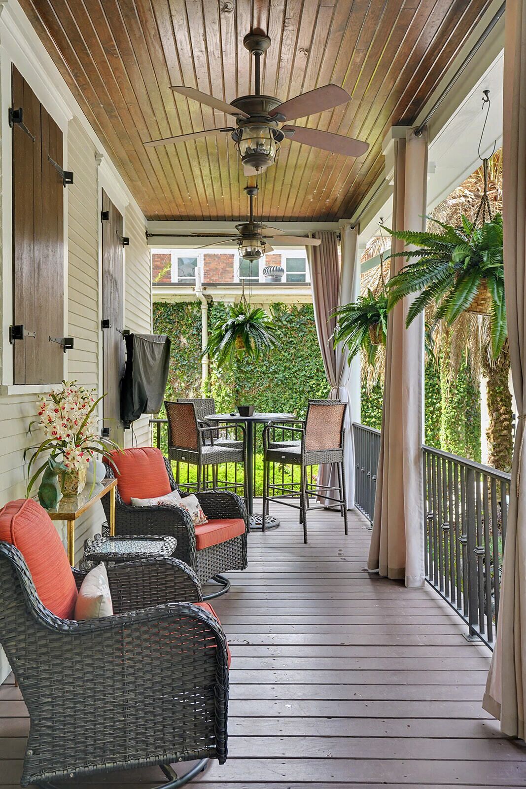 A covered porch with wicker furniture, a ceiling fan, and potted plants.