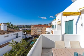 Ein Balkon mit Blick auf eine Stadtansicht, ein Pool und ein Gebäude mit weißer Fassade und grünen Fensterläden.