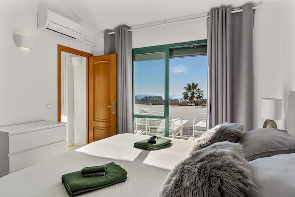 Ein Hotelzimmer mit Bett, Meerblick, einem Balkon mit Stühlen und einer Holztür.