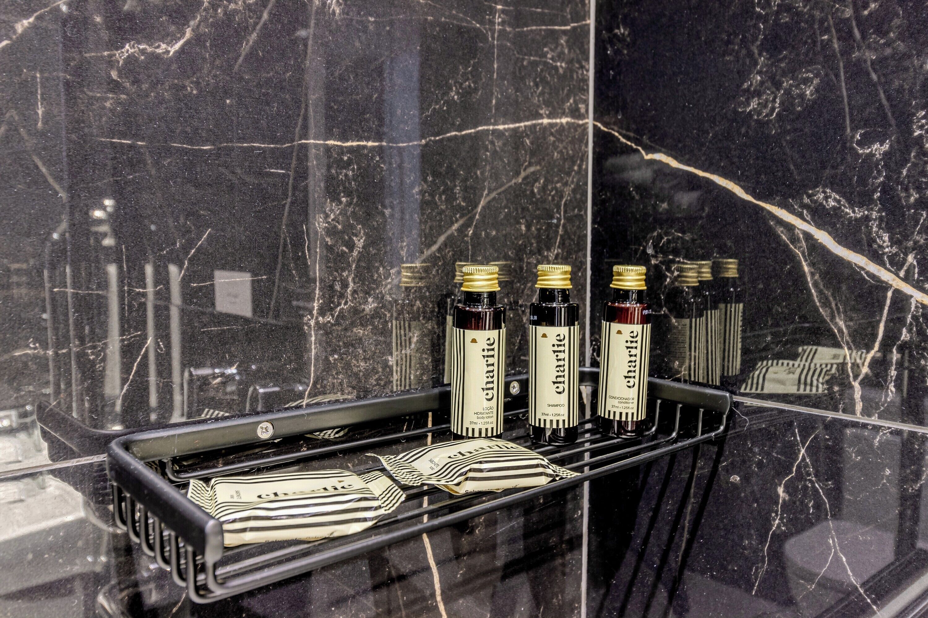 Une salle de bain avec un lavabo en marbre noir et une étagère où sont posés des flacons de shampoing et d’après-shampoing de la marque Charlie.