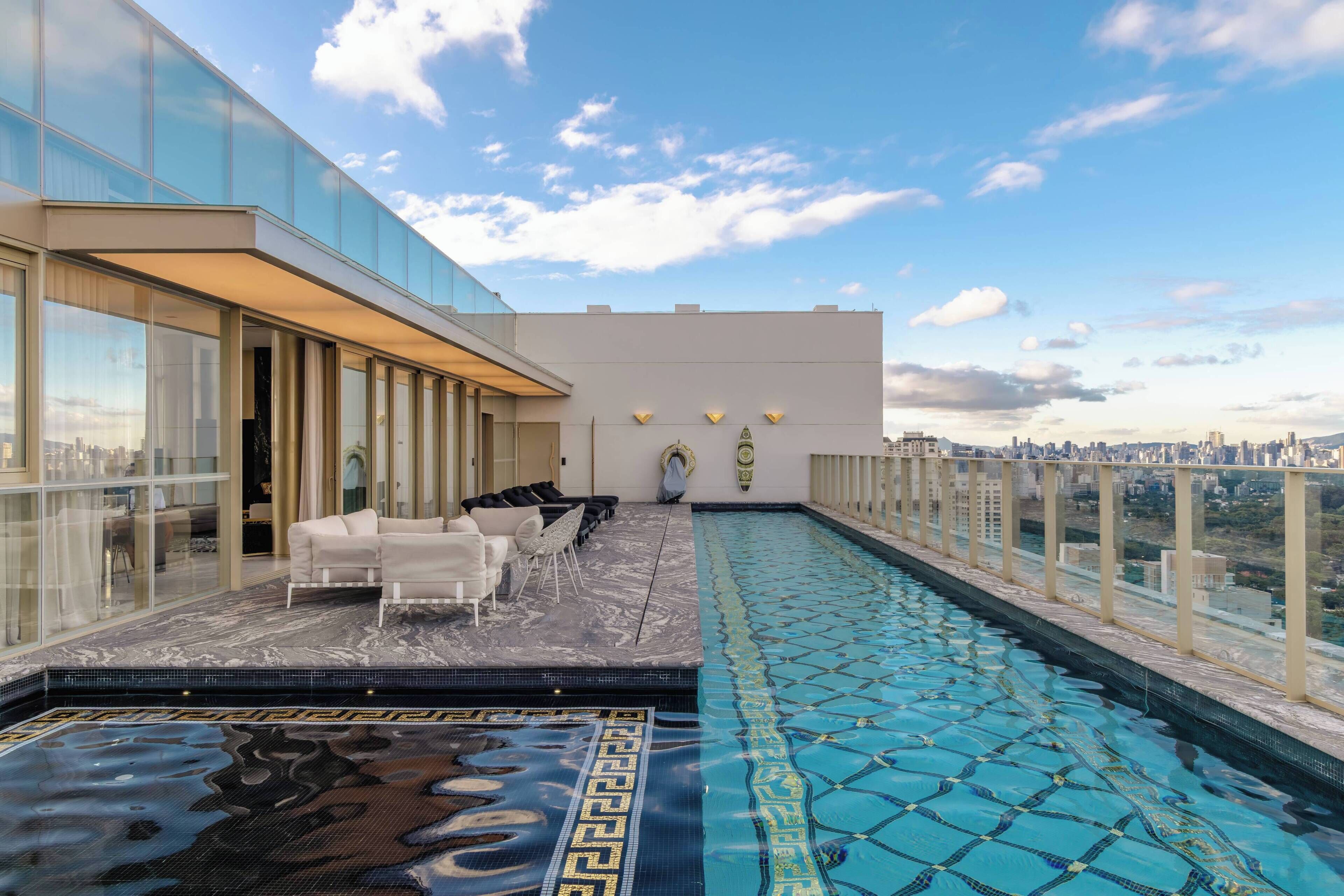 Une piscine sur le toit, protégée par une structure en verre, avec un espace salon et une vue sur la ville.