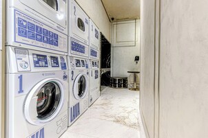 A laundry room with multiple washing machines, a marble floor, and a small table with a chair.