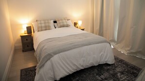 A neatly made bed with a white comforter and two pillows, flanked by bedside tables with lamps. A patterned rug is visible under the bed. - 3BR Stays 10 Mins from Legoland/Ascot/Heathrow - Free Wi-Fi/Parking (Windsor)