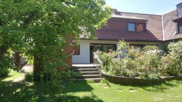 A house with a red-tiled roof, a front porch, and a garden with various plants.