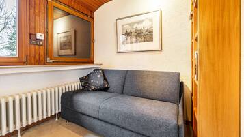 A room with a grey sofa, a framed picture on the wall, a window with a view, and a wooden cabinet.